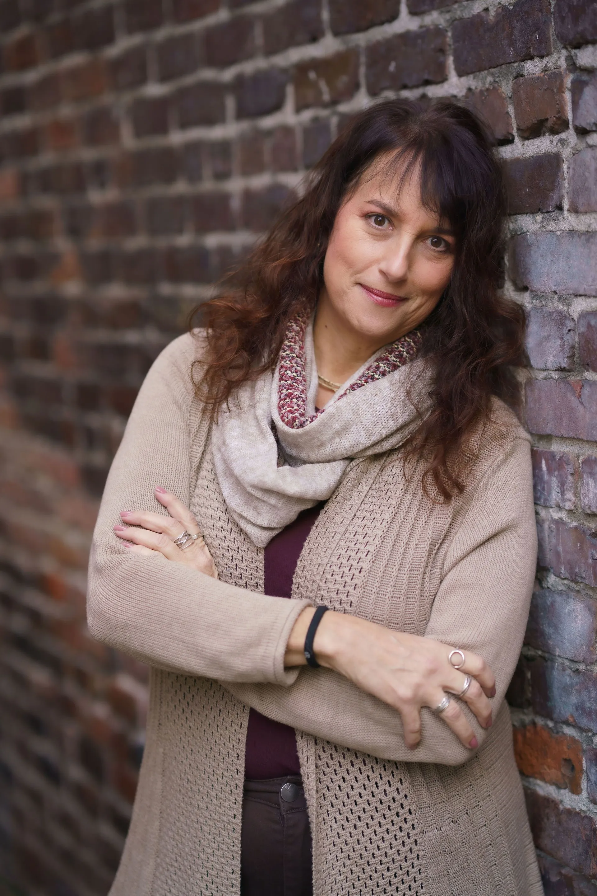 Issy Kleiman, MA, LMFT, standing with folded arms against a brick wall