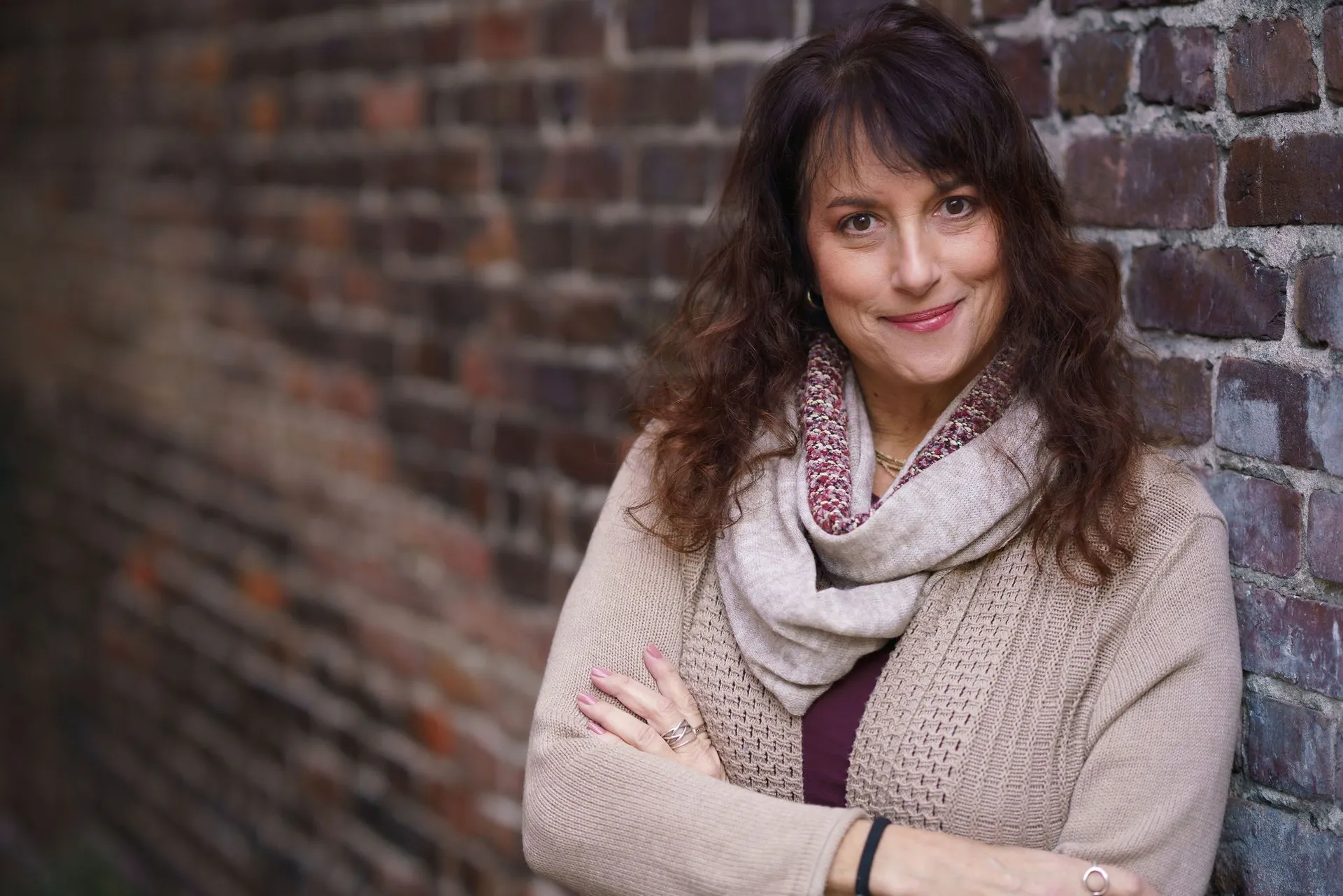 Issy Kleiman, MA, LMFT, AAMFT Approved Supervisor, smiling warmly in front of a brick wall, wearing a camel cardigan and scarf