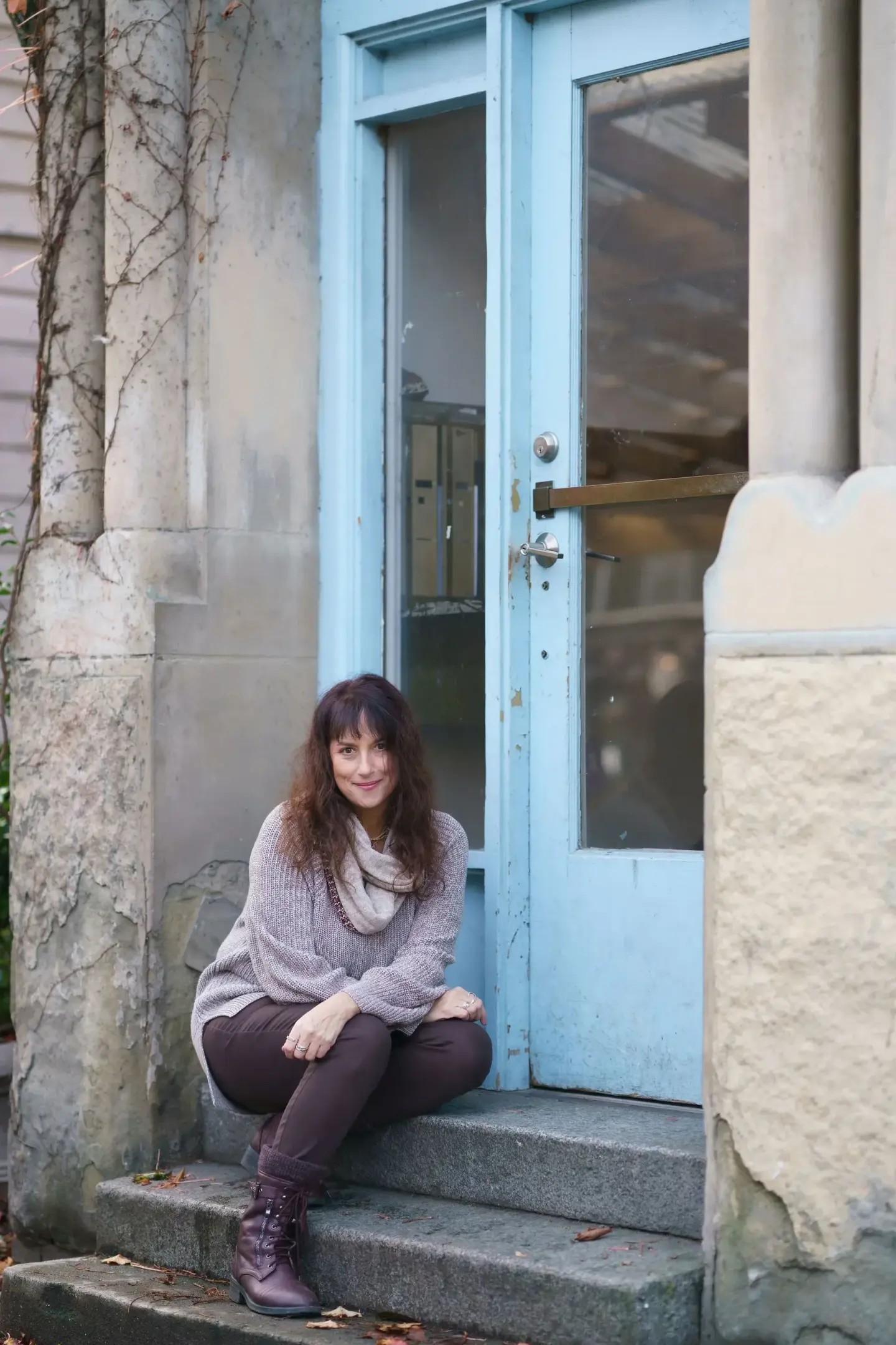 Issy Kleiman, MA, LMFT, AAMFT Approved Supervisor, seated on the front steps beside a pale blue door