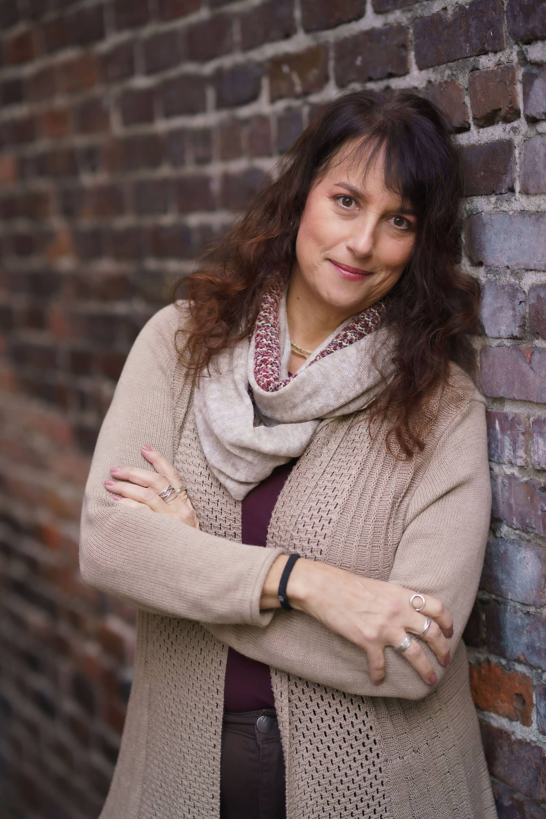 Issy Kleiman, MA, LMFT, standing with her arms crossed against a brick wall in a camel cardigan.